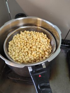 圧力鍋の中にざるに入った蒸し大豆